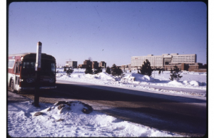Image of a bus stopping on the road with snow on the ground and the Ross Building in the distance.