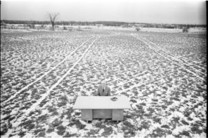 Man sitting at a desk in the middle of an empty field.